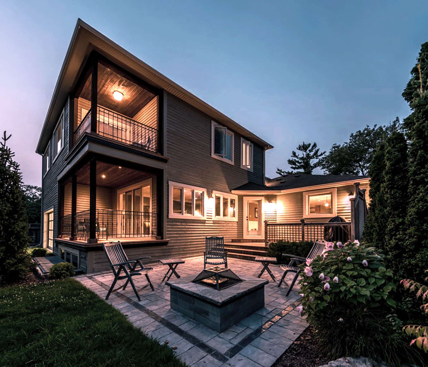 Two storey custom home with covered porches and stone fire pit patio at dusk, built by Revel Homes near Meaford