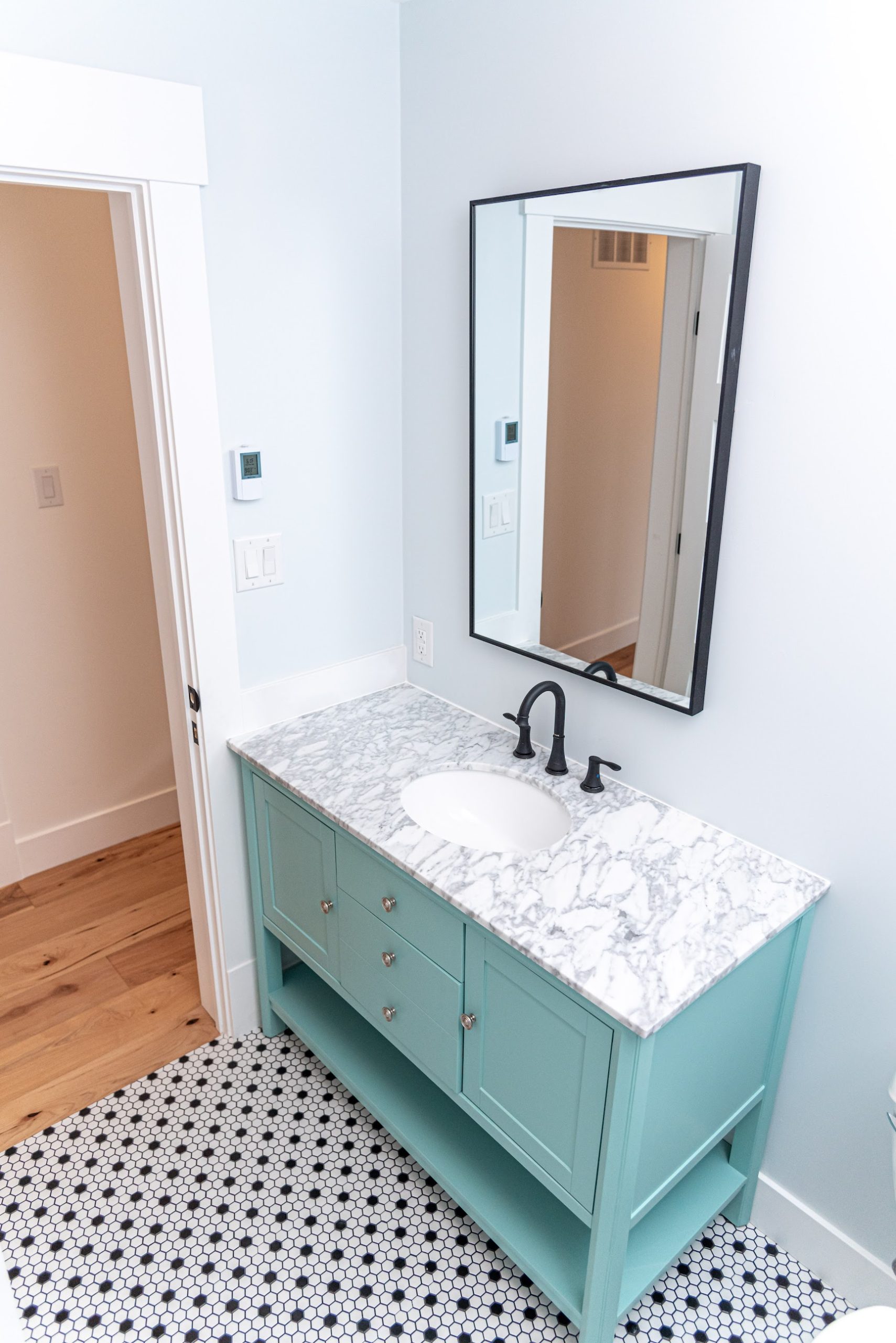 Powder room with pastel vanity, marble counter and hex tile floor by Revel Homes, serving Creemore