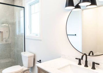 Bathroom renovation with round mirror and black fixtures by Revel Homes